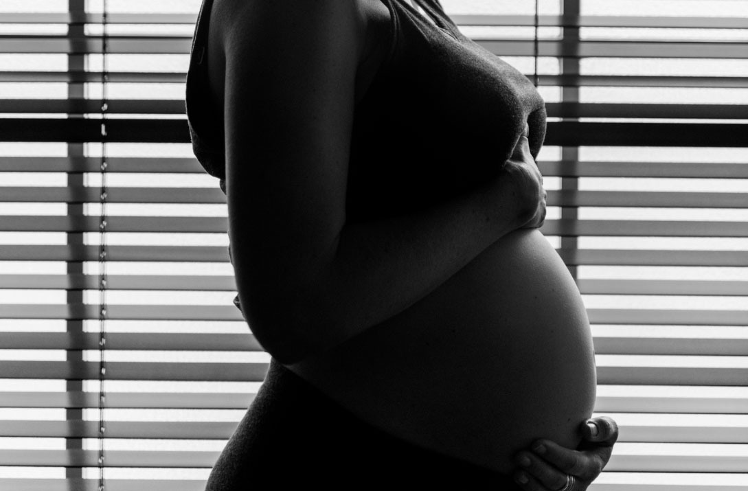 photo en noir et blanc de femme enceinte entourant son ventre arrondi de ses 2 mains