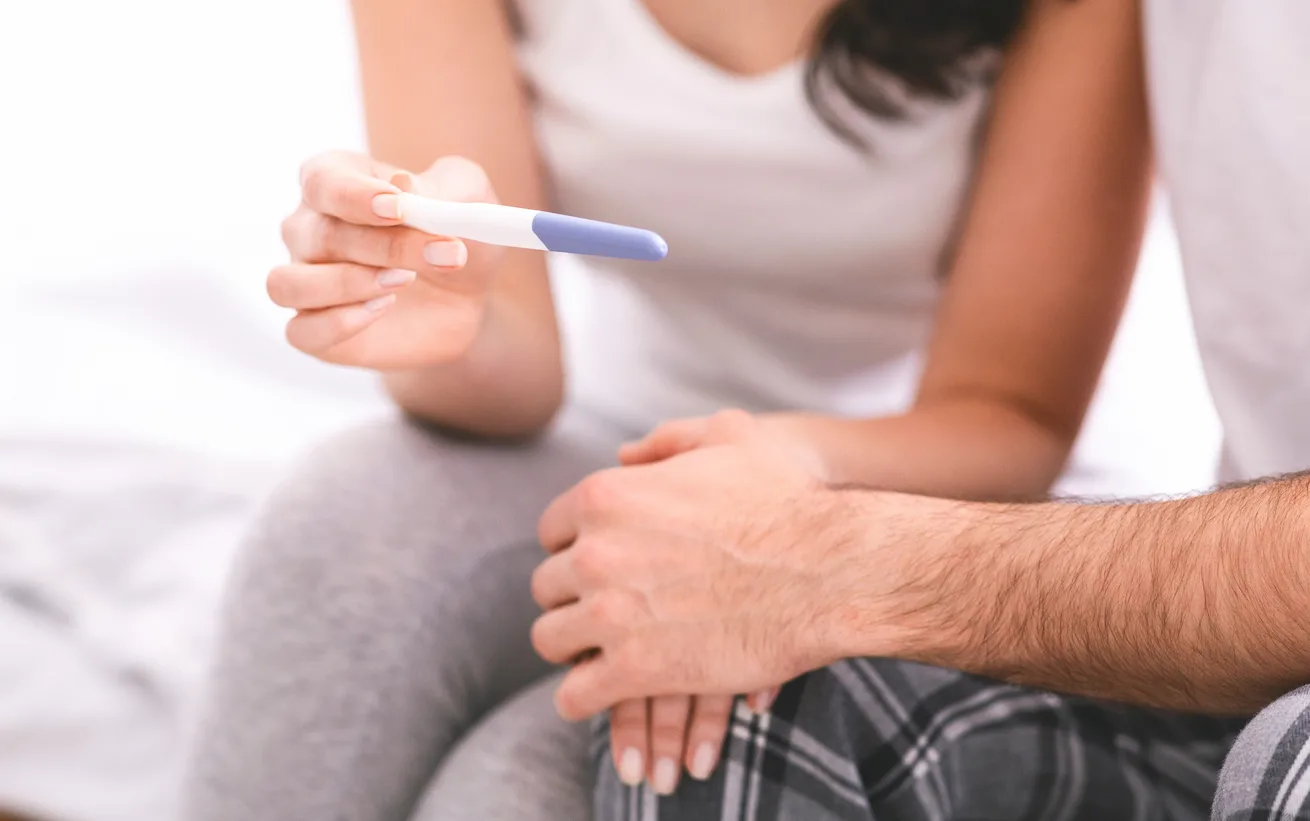 photo d'une femme qui tient un test de grossesse dans la main et de son conjoint qui lui tient l'autre main