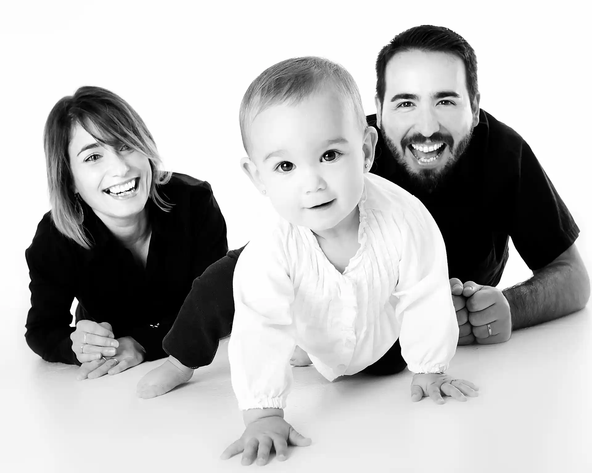Photo de famille en noir et blanc avec une femme, un homme et un bébé allongé sur le ventre et souriants